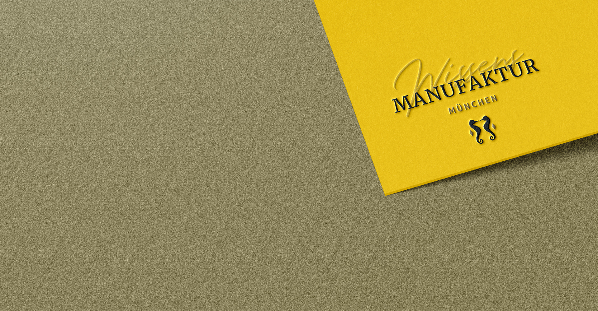 Banner der WissensMANUFAKTUR München mit geprägtem Branding auf gelbem Papier vor goldener Papierstruktur